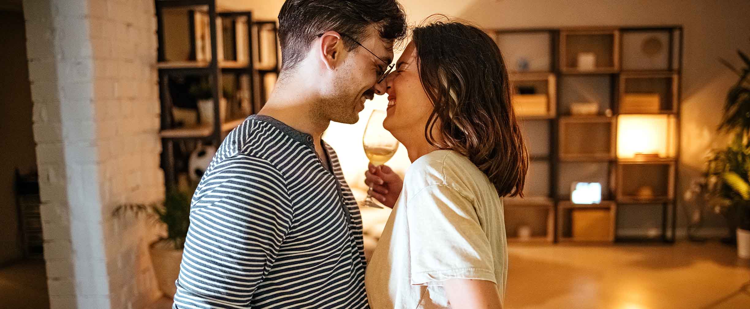 A young man and woman laugh as they touch their noses together while enjoying a drink together