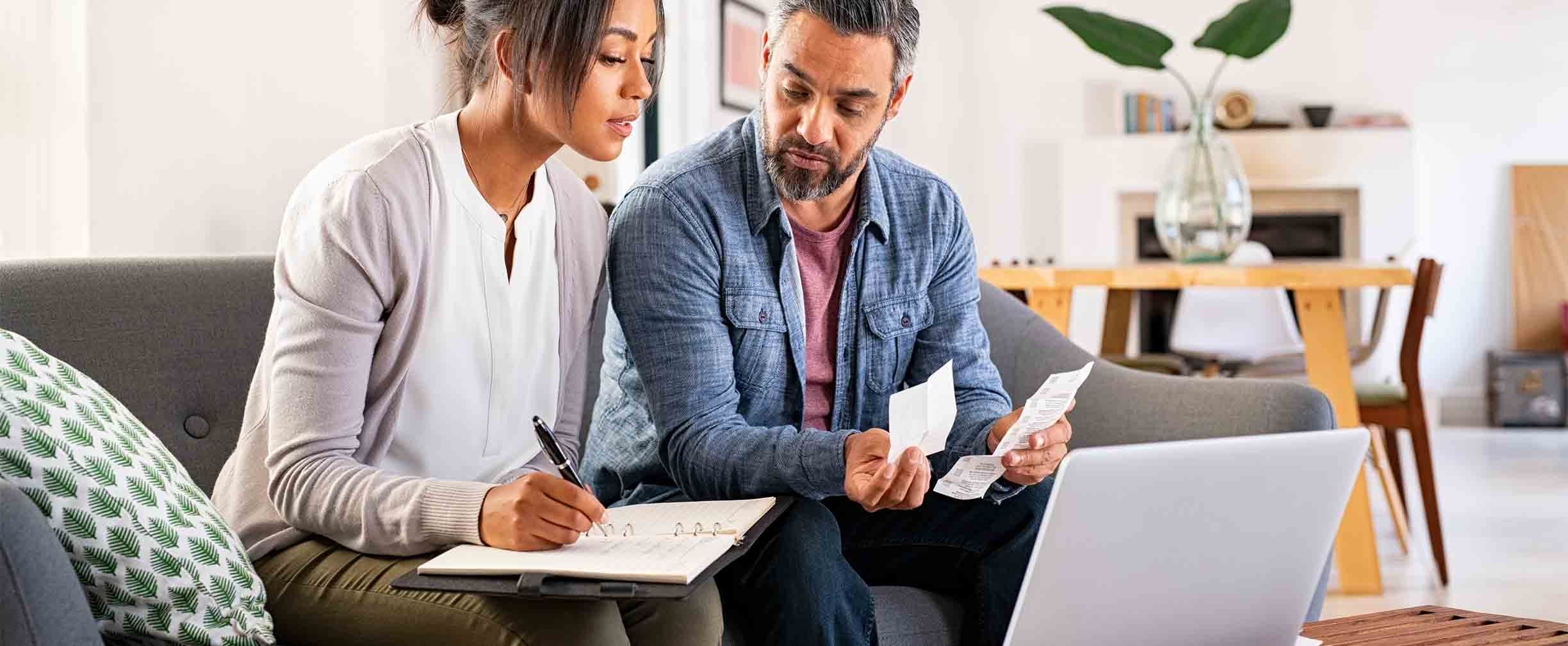 Mature couple calculating bills at home using laptop and calculator.