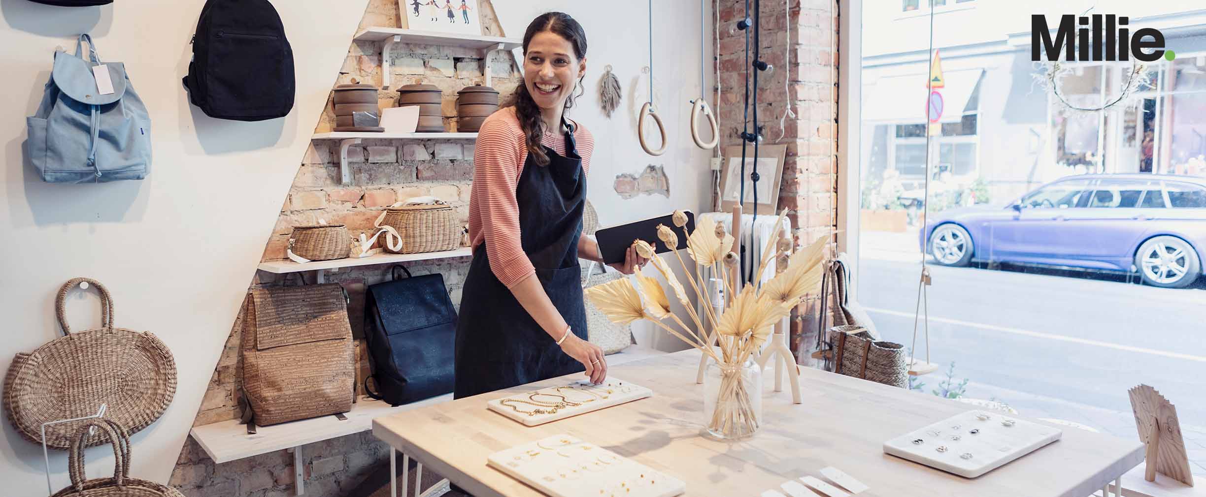 A photo of a female small business owner smiling in her shop of crafts, bags and jewelry.