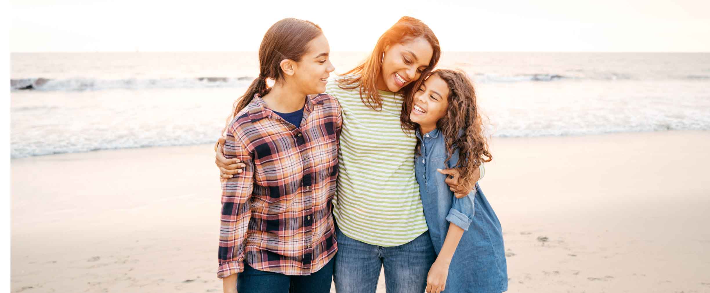 mother hugging her two daughters on the beach