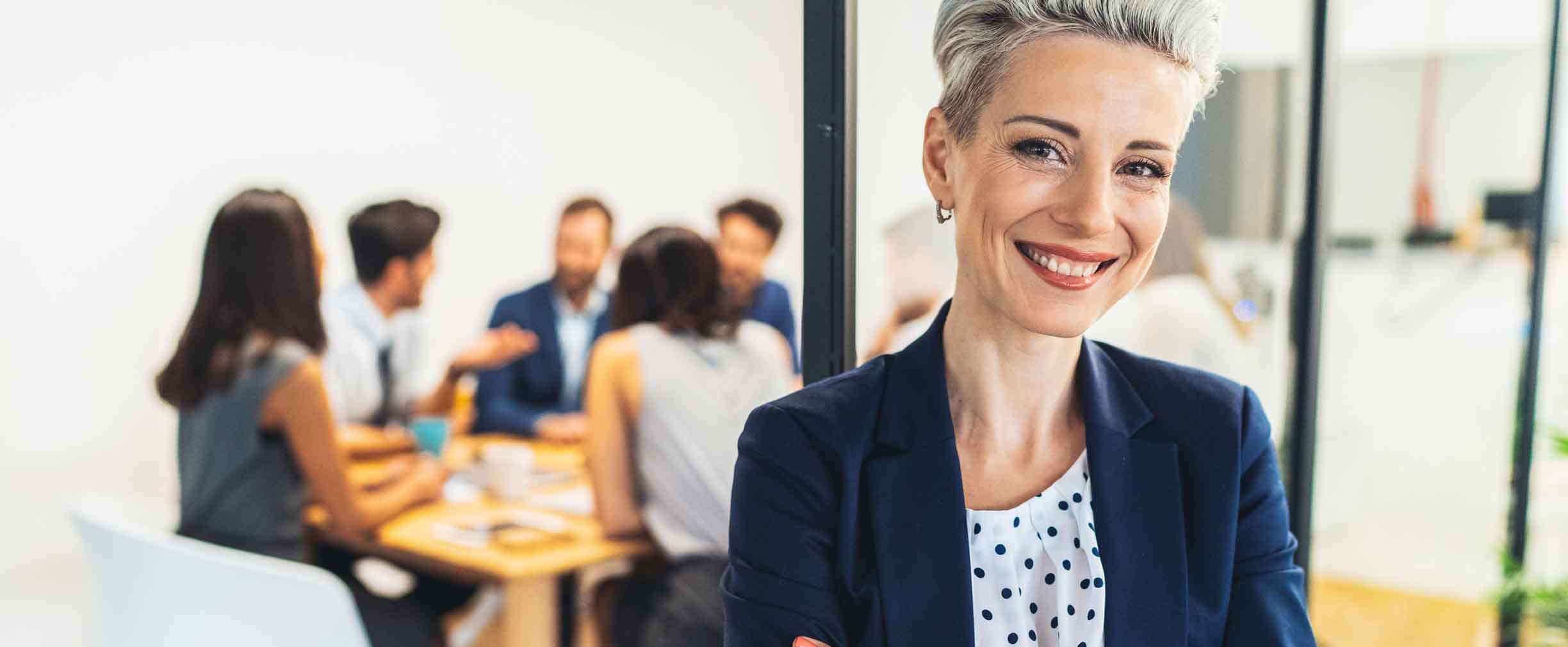 smiling female employee standing in front of coworkers in a meeting