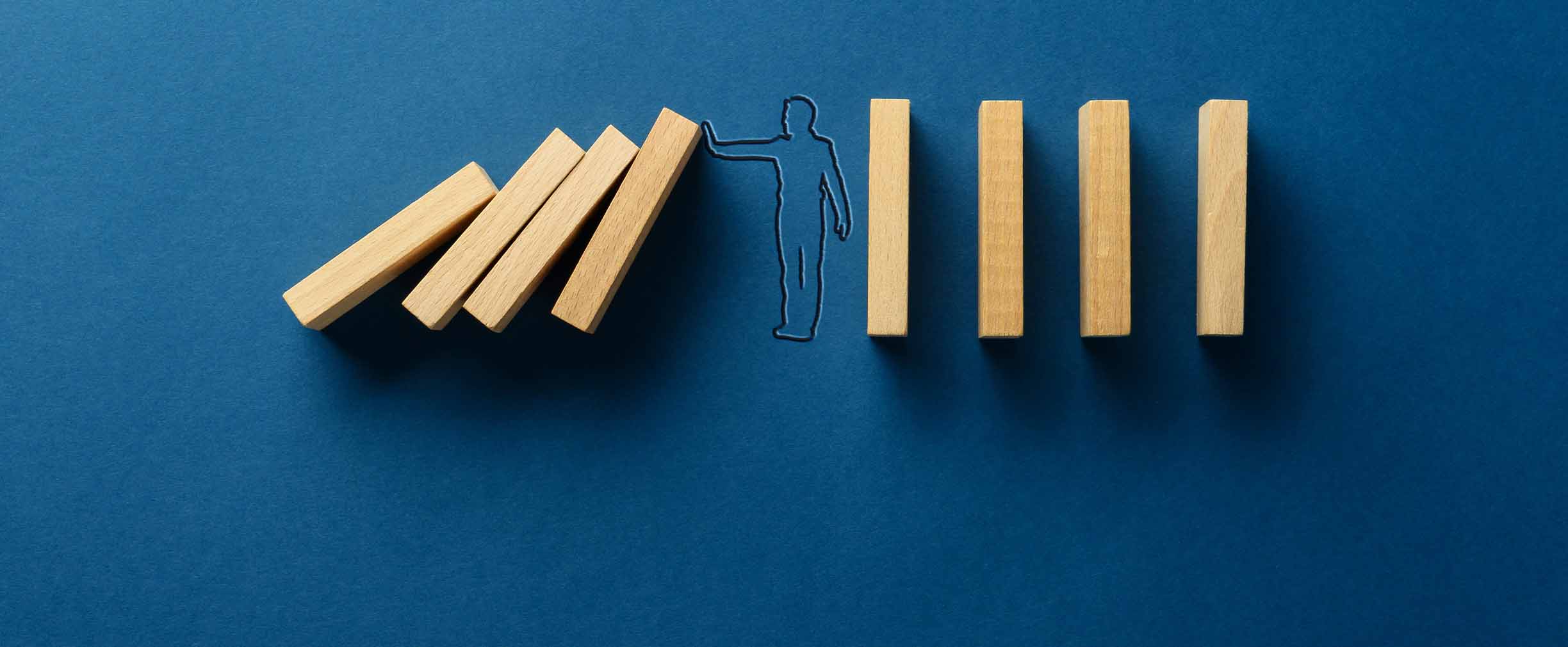 A photo illustration of a figure stopping a row of wooden dominos from falling